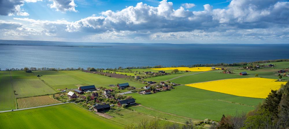 Swedish landscape by lake Vättern with blue sky, green and yellow fields, farms, and some forest.